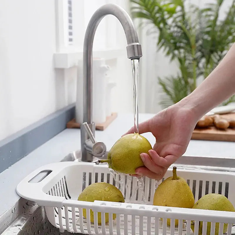 Kitchen drain basket with adjustable rack in sink; white, four pears being rinsed under running water