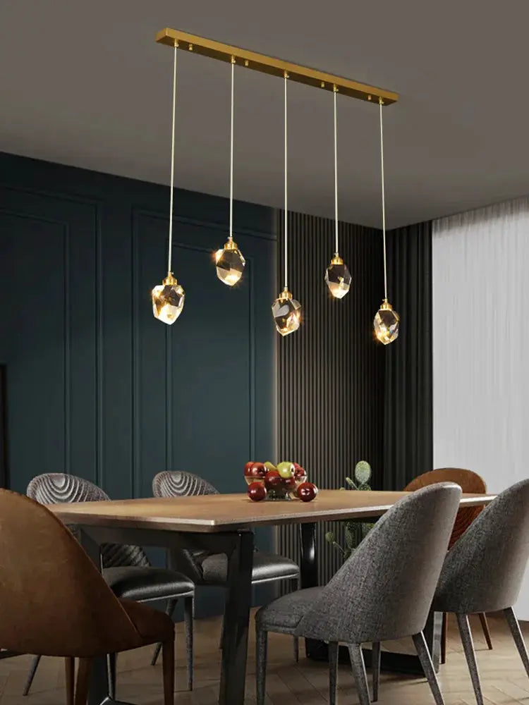 Ceiling pendant lamp by Simples Market with five crystal pendants on a gold bar, modern Nordic dining room chandelier.