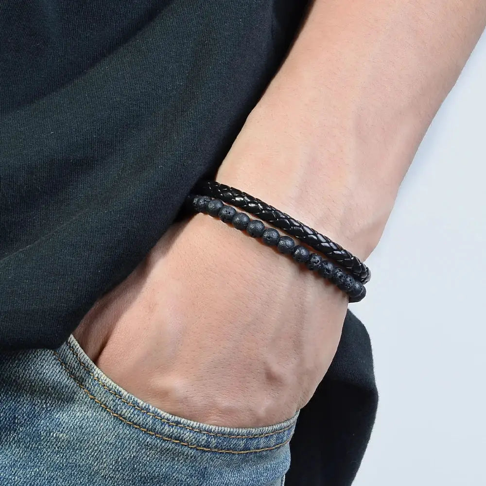 Two black bracelets on the wrist: a braided leather-style band and a beaded stone bracelet