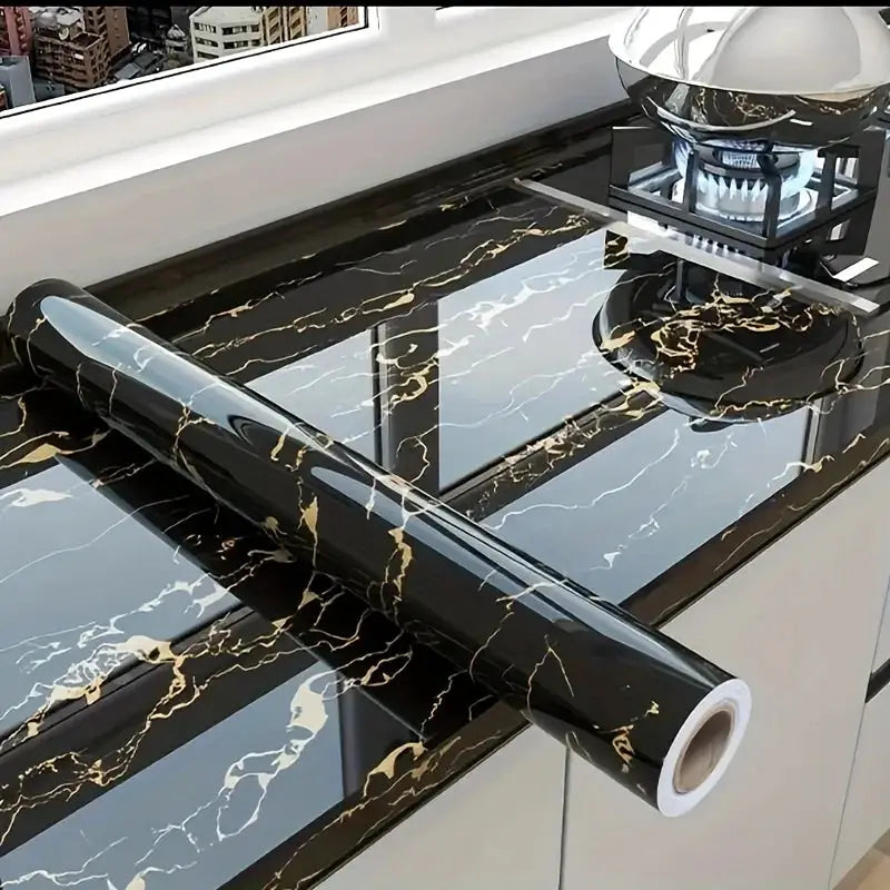 Self-adhesive black marble wallpaper roll with gold veins being applied to a kitchen countertop.
