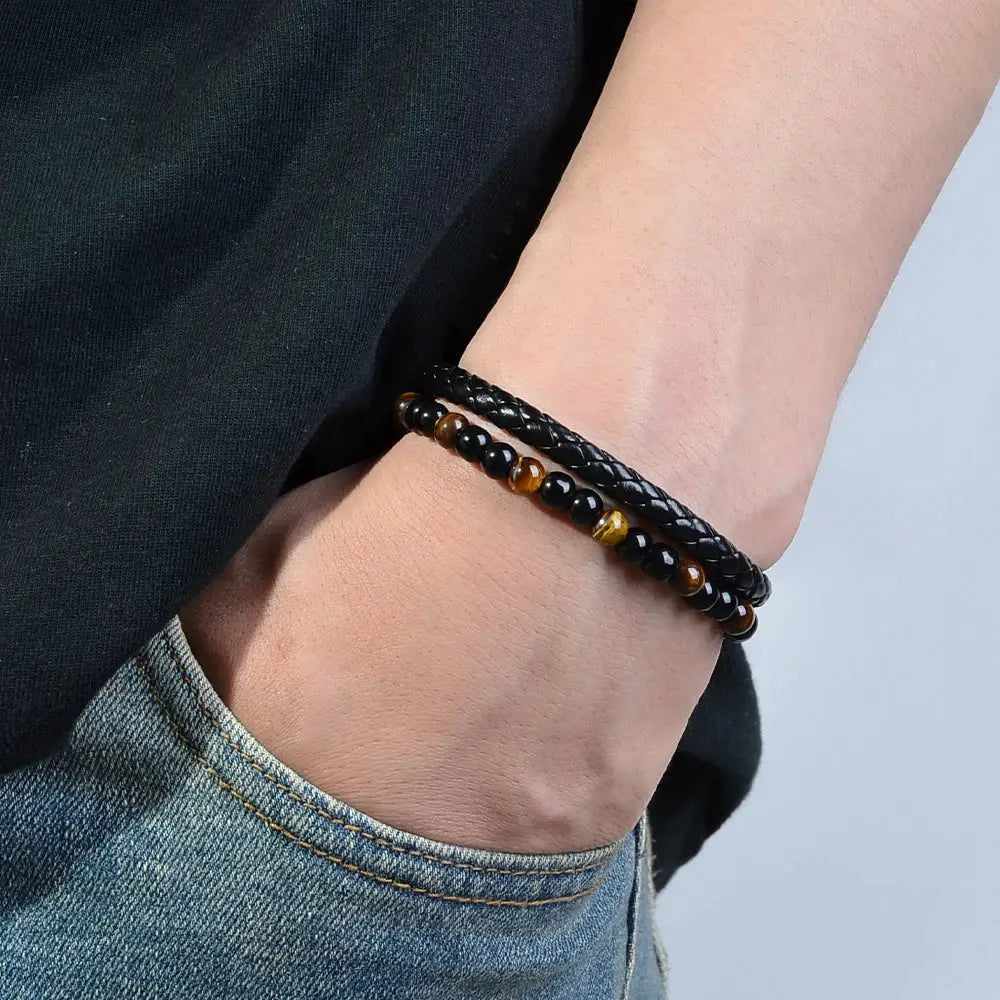 Two bracelets on the wrist: a black braided band and a tiger eye lava stone bead bracelet