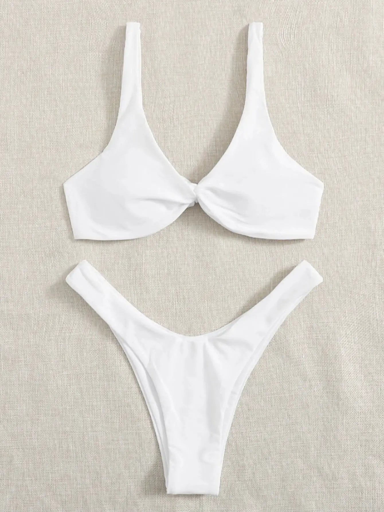 White two-piece bikini set with twist-front padded top and high-leg bottoms on beige fabric.