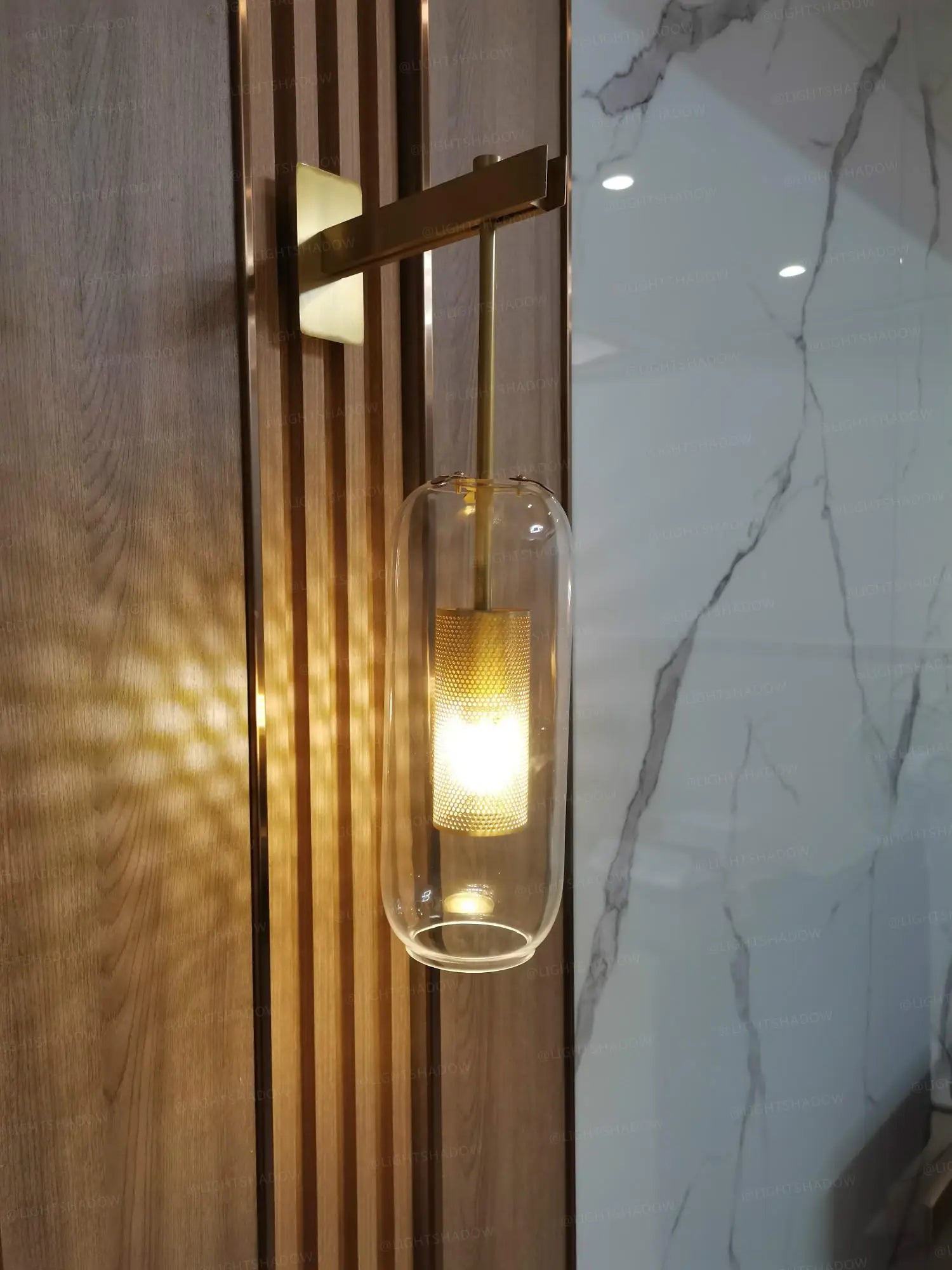 Modern glass wall light sconce with brass finish and cylindrical glass shade mounted on wood panel