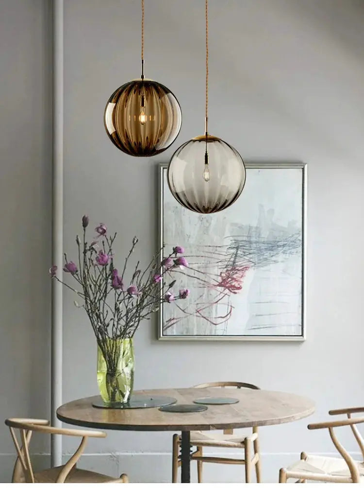 Two modern LED glass ball pendant lights, amber and clear brown-tinted spheres, hanging over a dining table