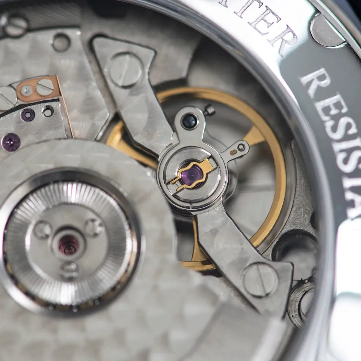 Sugess men's watch movement close-up in stainless steel, showing gears, balance wheel and purple jewels