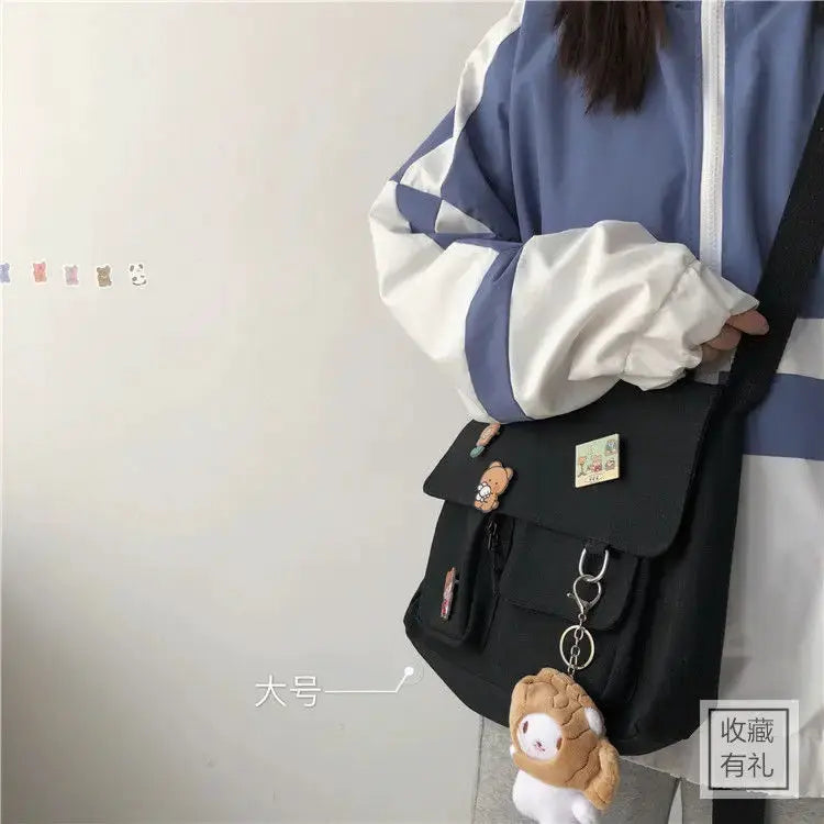Women's black canvas messenger bag by Simples Market with flap, front pockets, and bear keychain.
