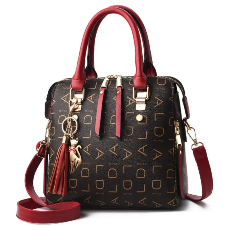 Black PU leather handbag with gold English-letter pattern, red top handles, crossbody strap, tassel and cat charm.