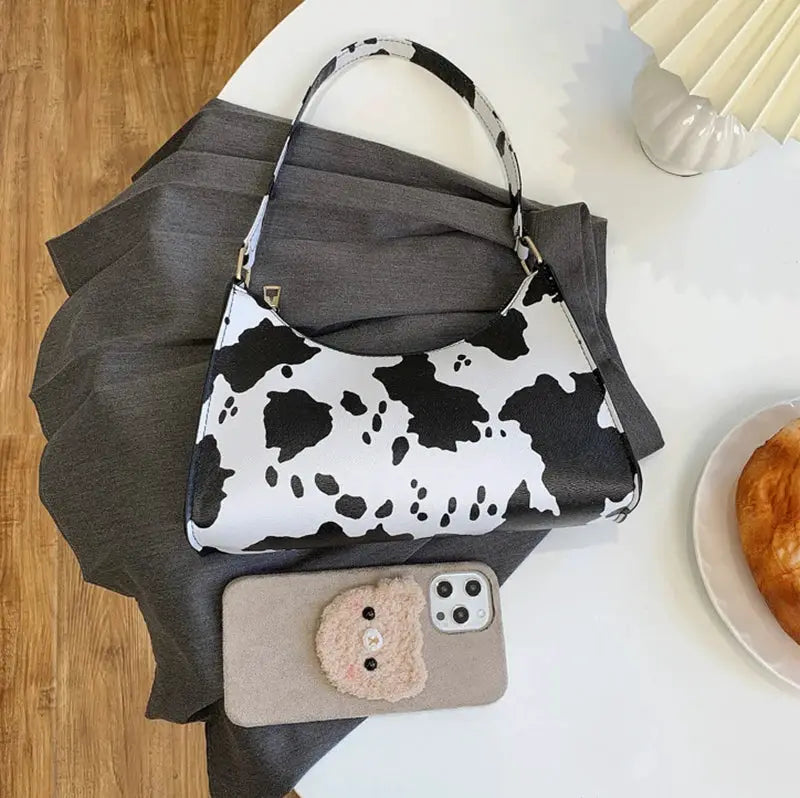 Simples Market cow-print PU leather shoulder bag with short handle and beige phone case nearby