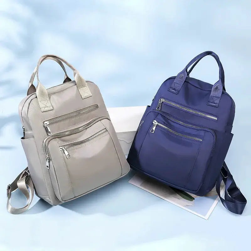 Two women's backpacks in beige and navy with multiple zip pockets and top handles