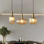 Retro glass pendant lights by Simples Market; three amber ribbed shades with brass tops over a dining table.