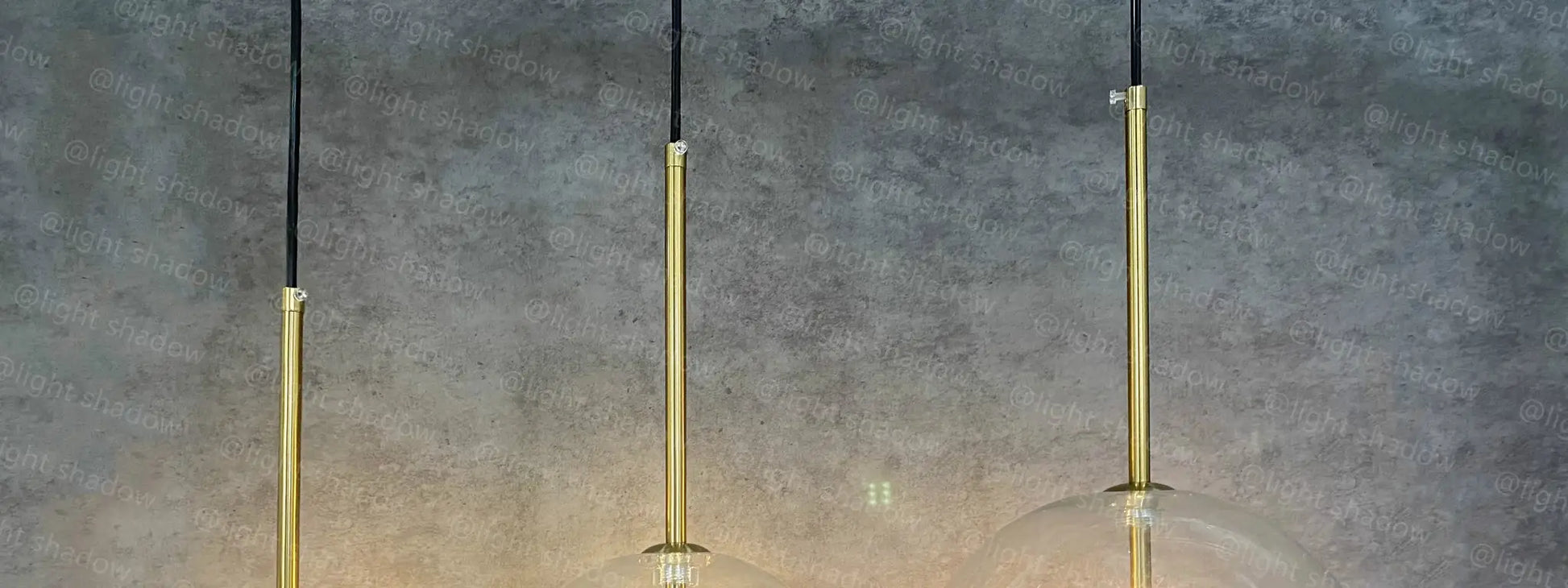 Three gold LED pendant lamps with glass globe shades on black cords by Simples Market