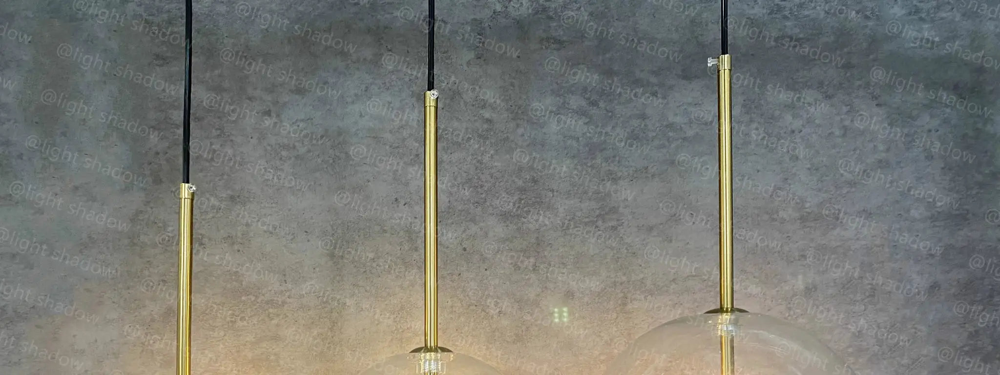 Three gold LED pendant lamps with glass globe shades on black cords by Simples Market