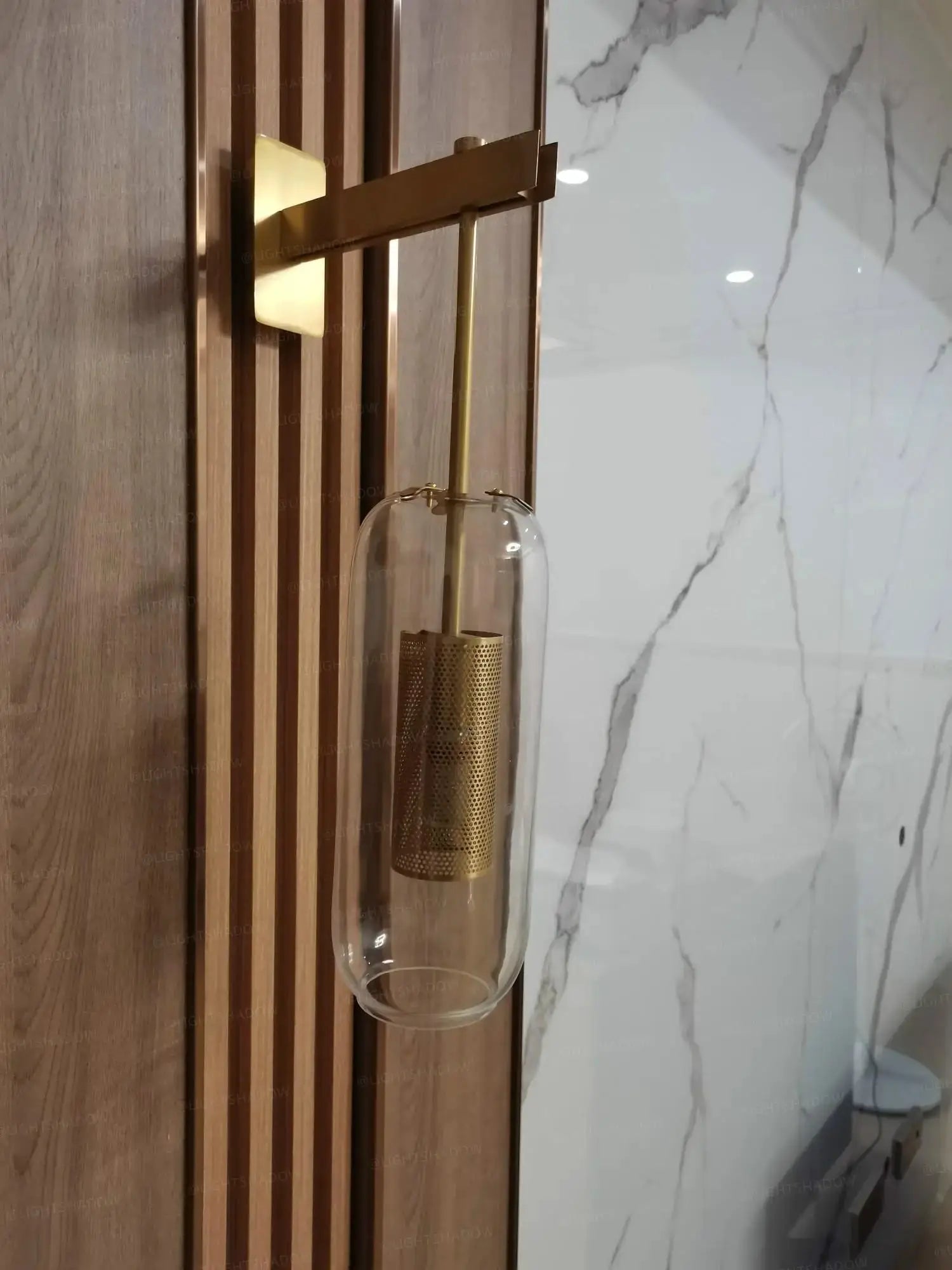 Modern glass wall light sconce with brass arm and clear cylindrical shade, LED fixture