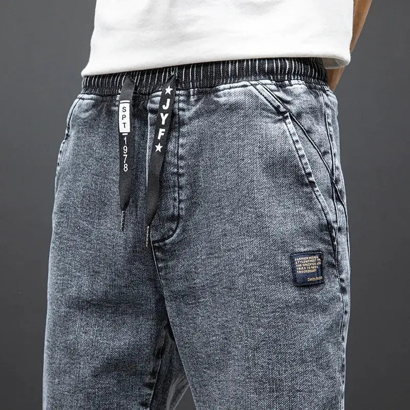 Men's cargo denim jogger jeans in dark blue wash with drawstring waistband and patch