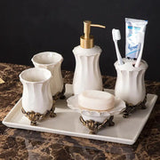 White ceramic bathroom set on a tray with bronze feet; includes dispenser, toothbrush holder, tumblers, soap dish.