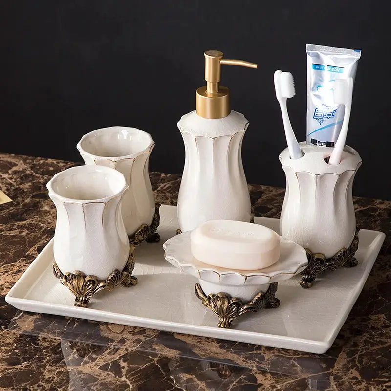 White ceramic bathroom set on a tray with bronze feet; includes dispenser, toothbrush holder, tumblers, soap dish.
