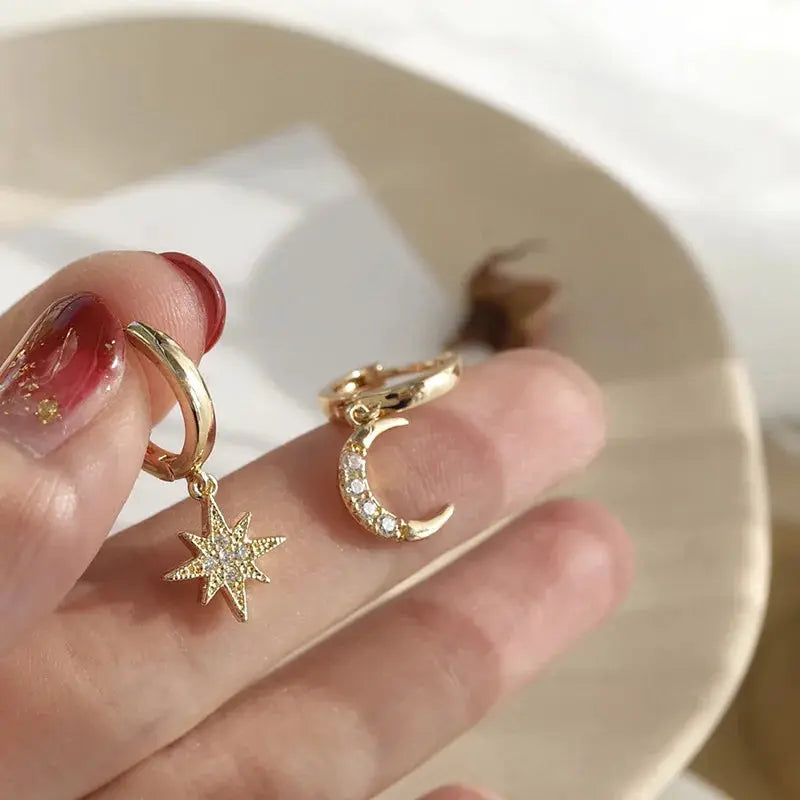 Geometric asymmetric star and moon dangle earrings pair in gold-tone with clear stones by Simples Market