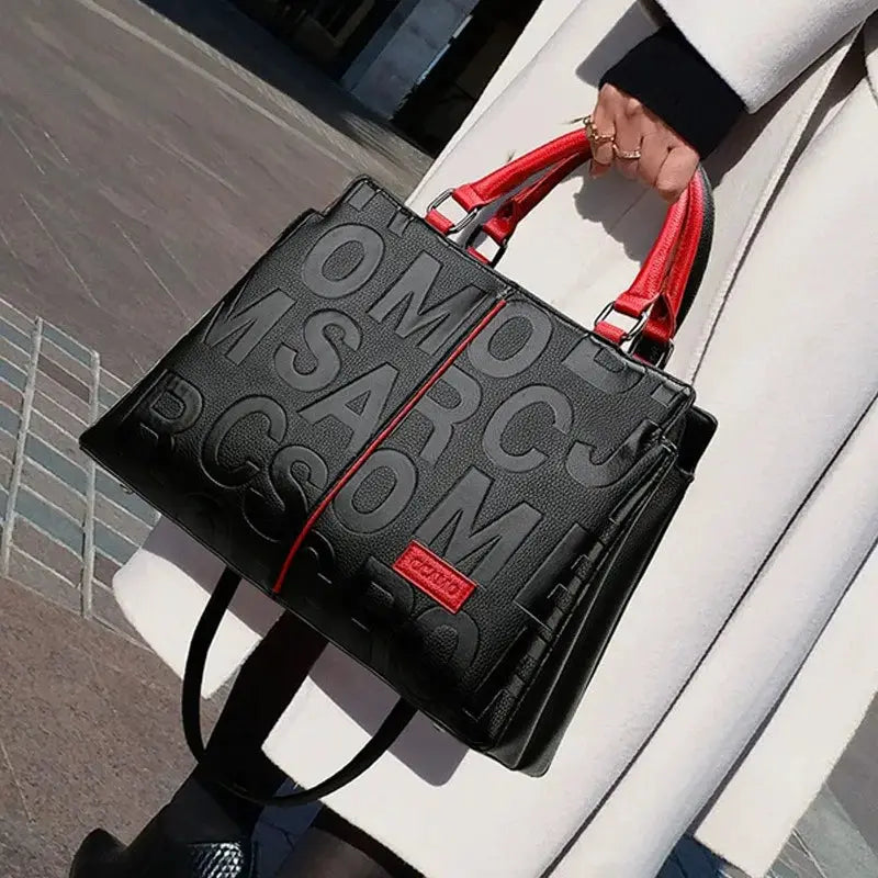 PU leather crossbody bag in black with red handles by Simples Market, embossed letter pattern.