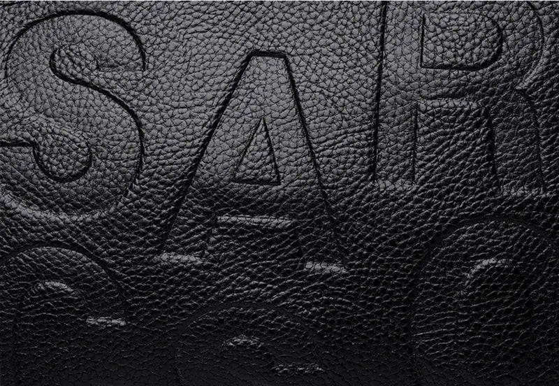 PU leather bag close-up with black pebbled texture and embossed lettering.