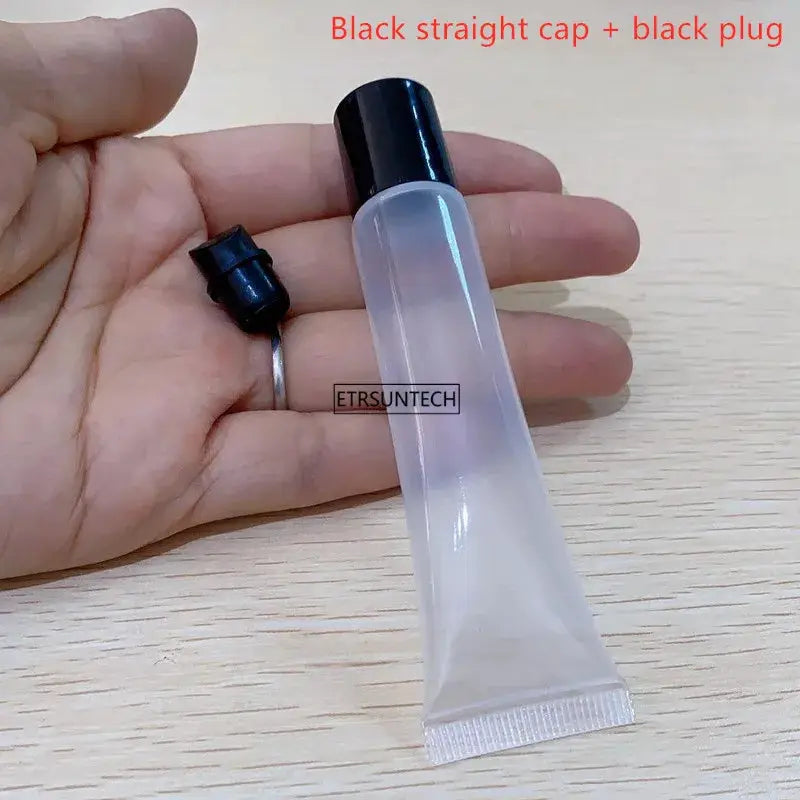 Clear plastic lip gloss container with black cap and black plug; empty squeeze bottle