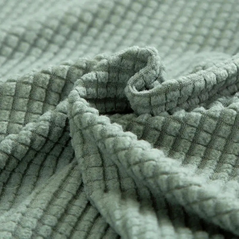 Thick sage green sofa protector with quilted jacquard grid for L-shaped couches.
