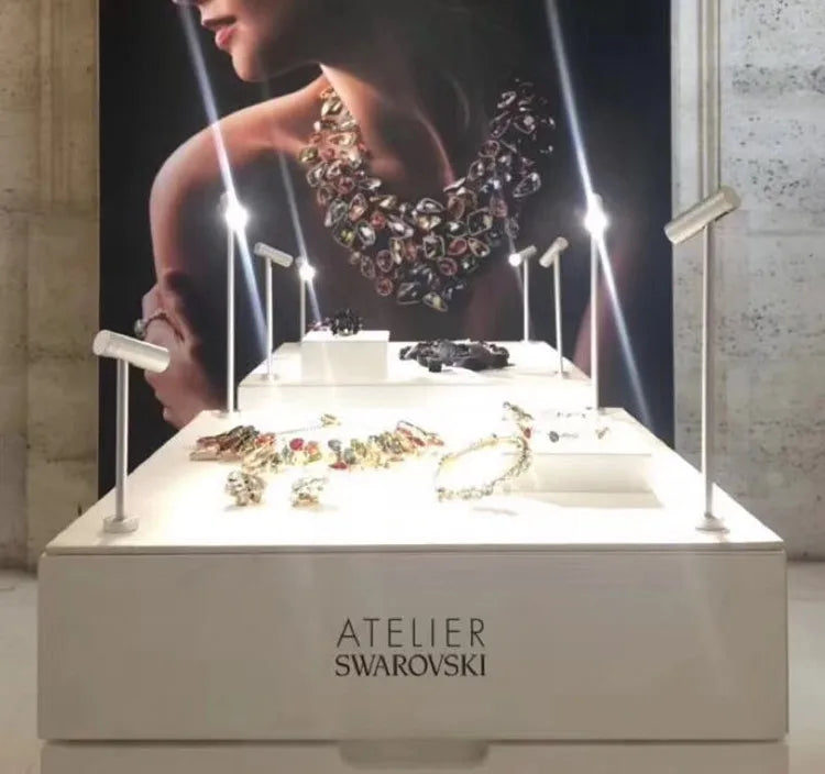 LED spotlight jewelry display lamp with rotatable posts on white counter; Swarovski Atelier signage