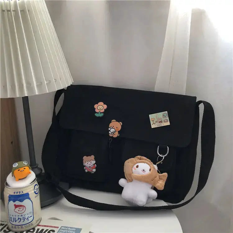 Women's black canvas messenger bag with cute cartoon patches and a plush keychain