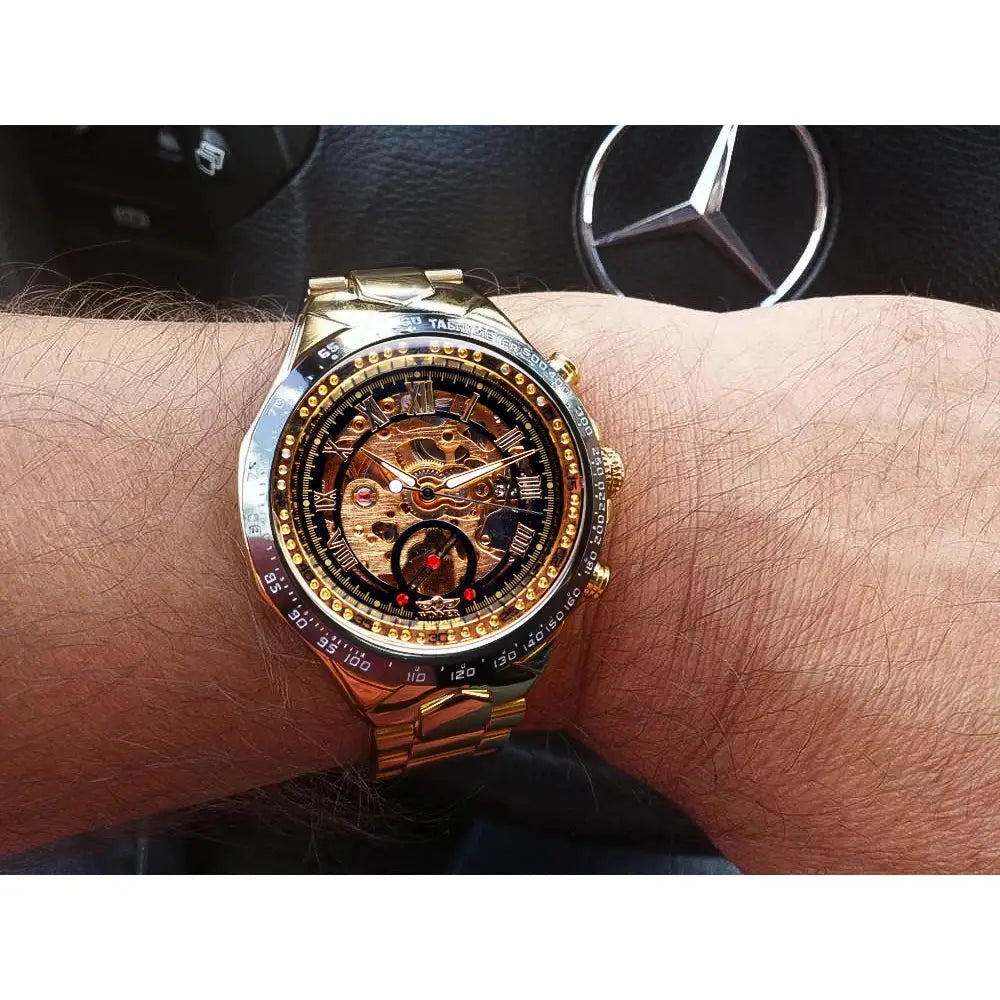 Winner mechanical skeleton watch on wrist; gold-tone bracelet with exposed gears and tachymeter bezel