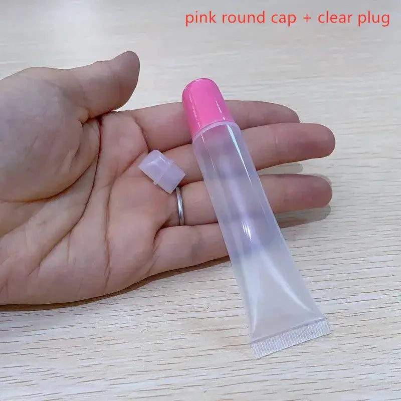 Lip gloss container with pink round cap and removable white plug, clear tube held in hand