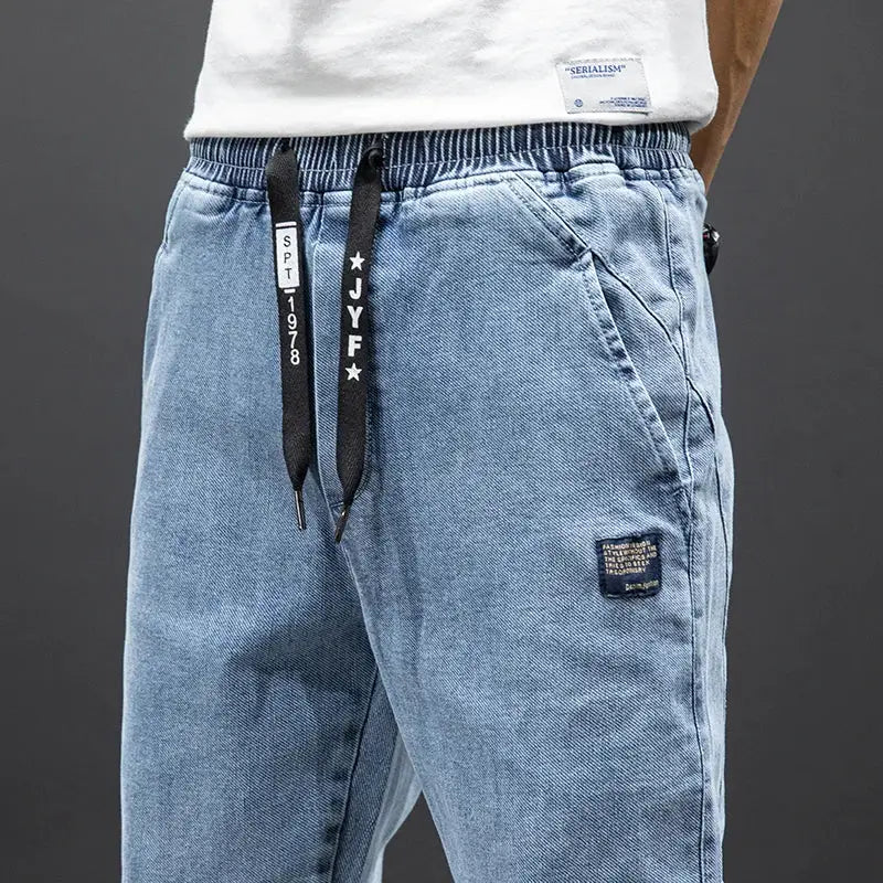 Men's light blue denim cargo jogger pants with elastic waistband, black drawstrings, baggy fit, thigh patch