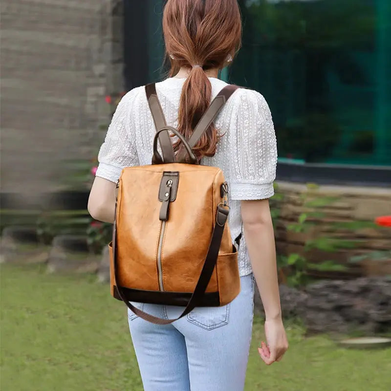 Anti-theft women’s backpack in tan PU leather with top handle and adjustable shoulder straps, large capacity.