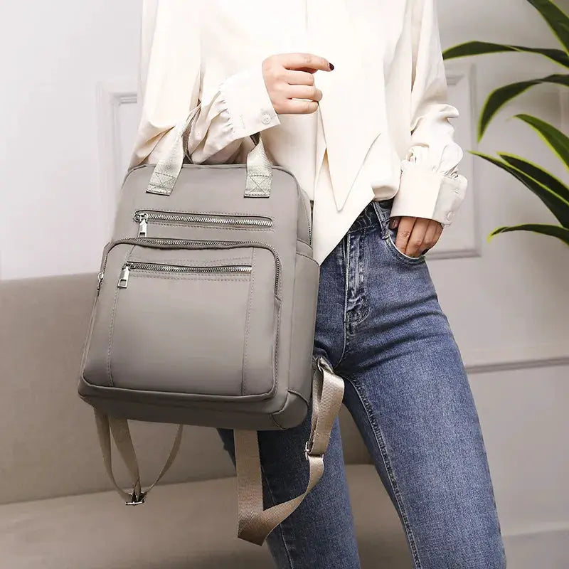 Gray women's Oxford backpack with multiple zip pockets and top handles.