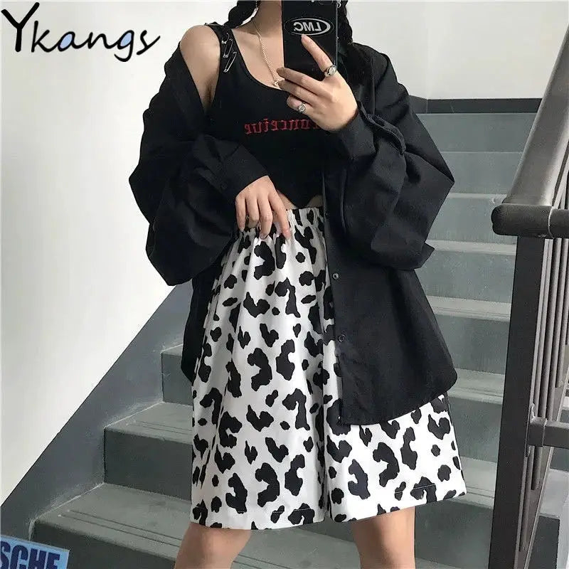 Women's three-piece outfit: black oversized shirt jacket, black crop top, and white cow-print skirt.