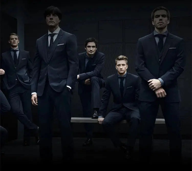 Group of men in black business suits posing in a dim, modern studio.