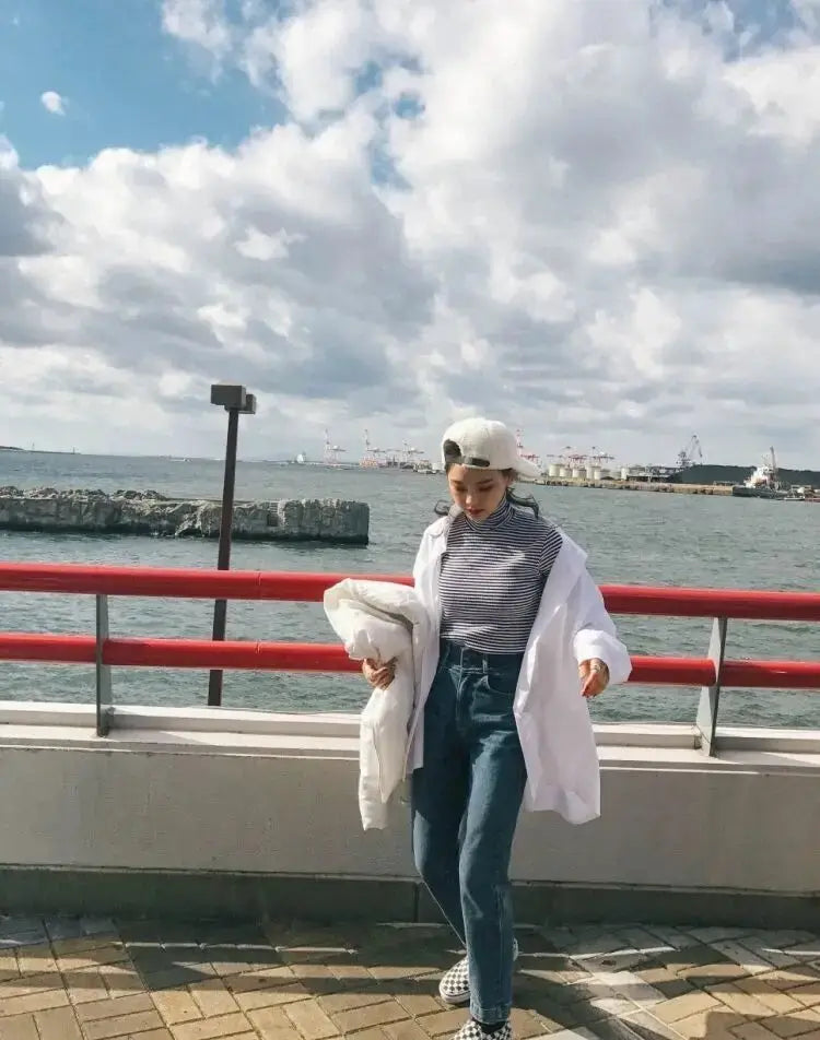 White oversized jacket worn by a woman with a striped top, jeans, and beret by the seaside.