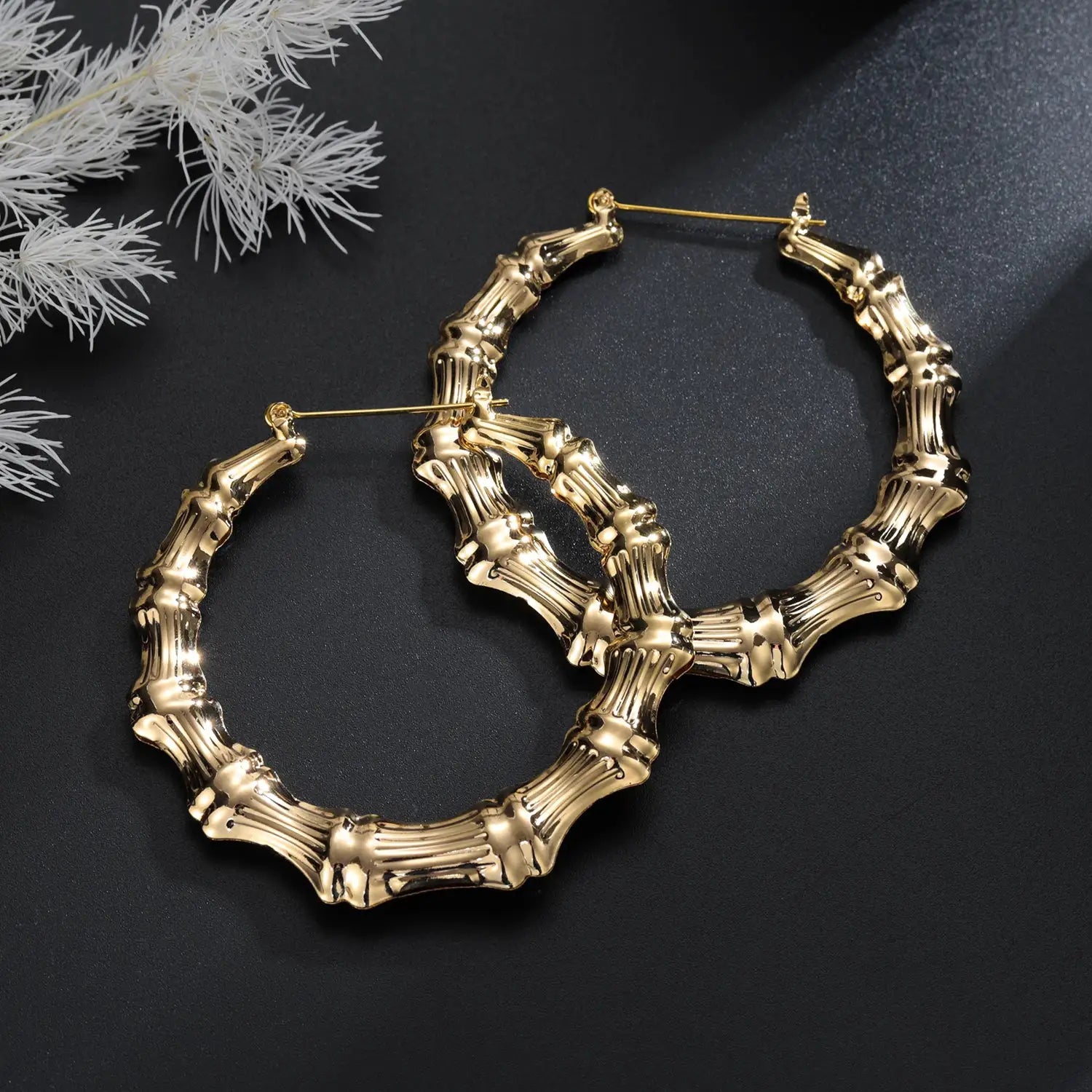 Gold-tone bamboo hoop earrings with chunky segmented design on dark background