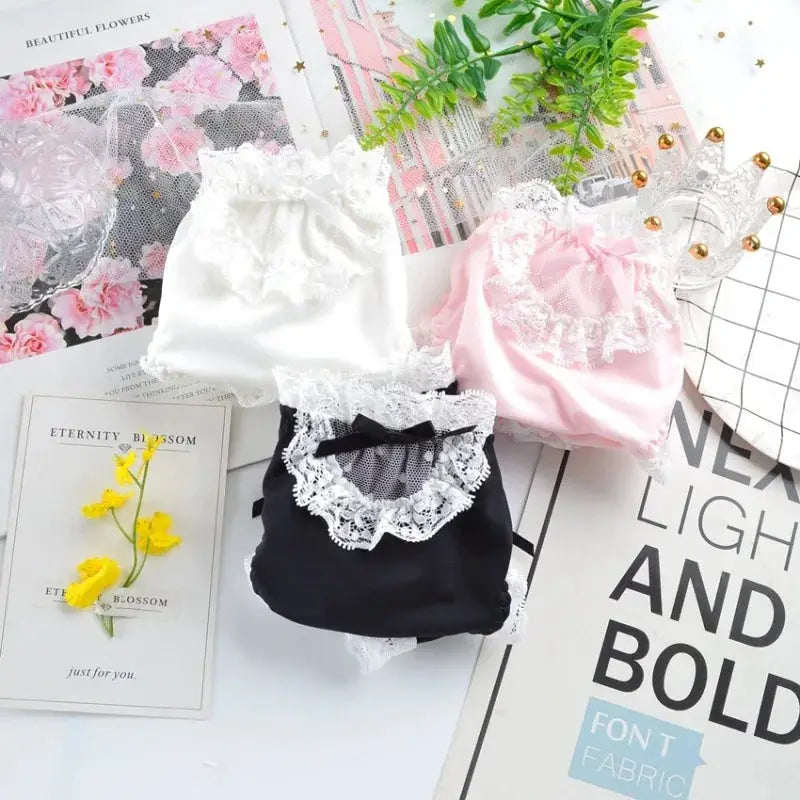 Three lace-trim panties in white, pink, and black with ruffled lace and bow details.