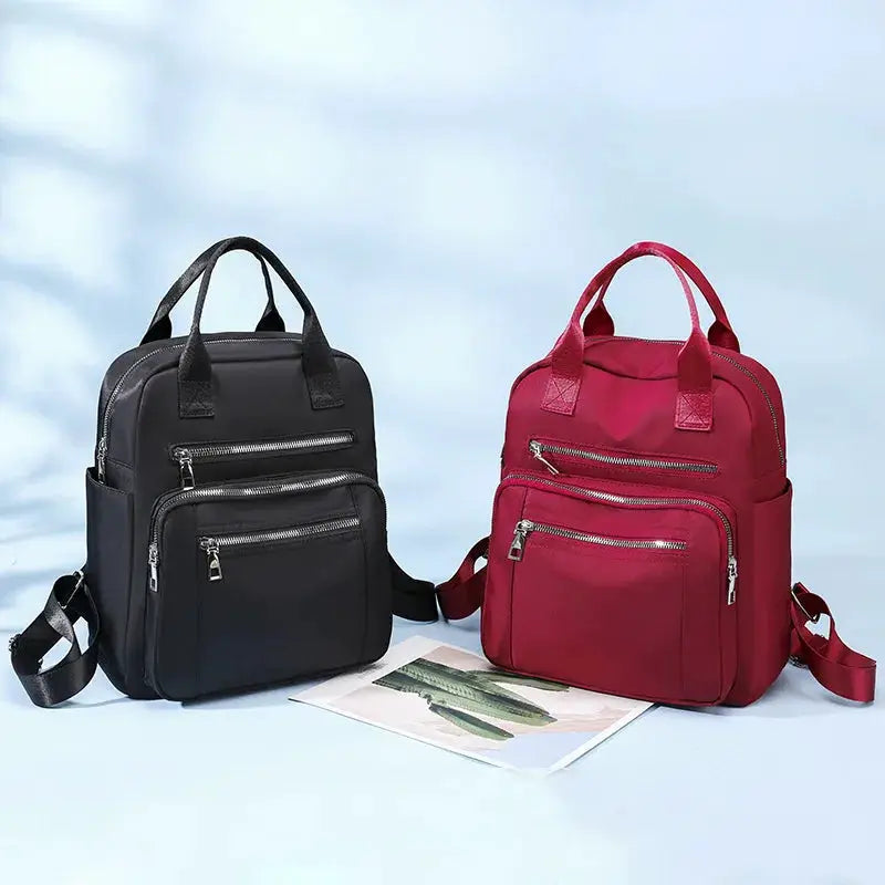 Two women's travel backpacks, black and red waterproof Oxford bags with multiple zip pockets