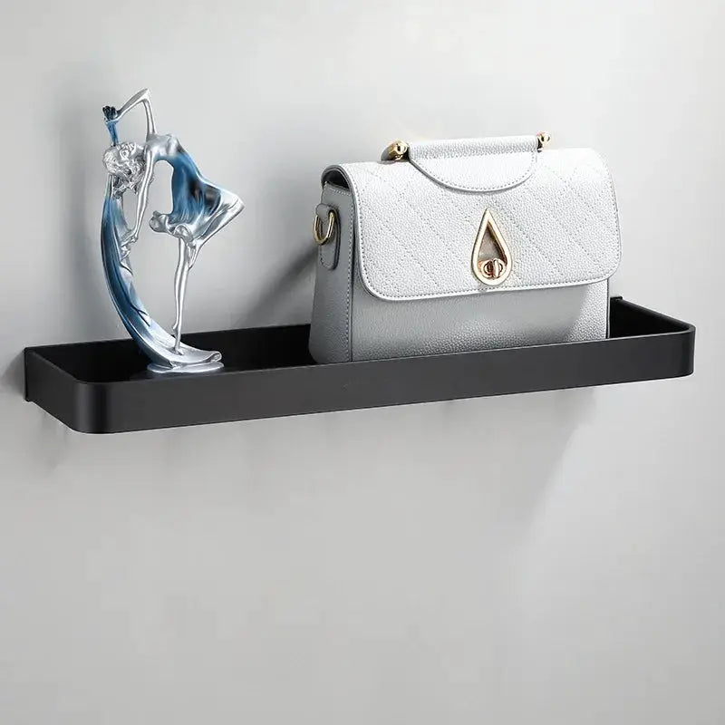 Bathroom wall-mounted black aluminum shelf with a gray quilted handbag and a decorative sculpture