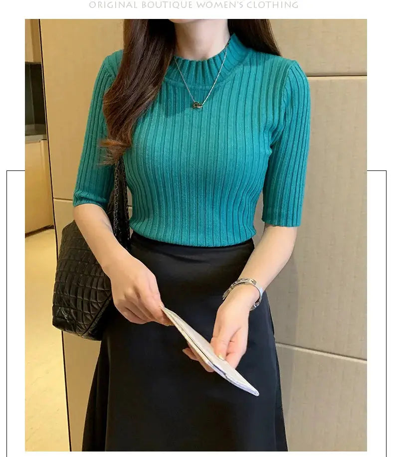Teal ribbed-knit short-sleeve blouse, paired with a black skirt and quilted handbag.