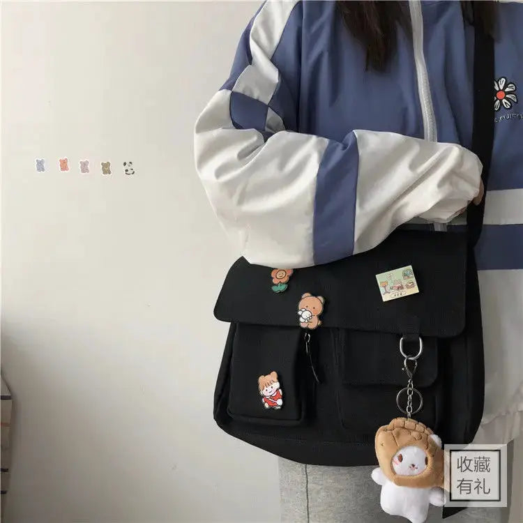 Women's black canvas messenger bag with front flap and pockets, decorated with cute bear patches and a keychain charm