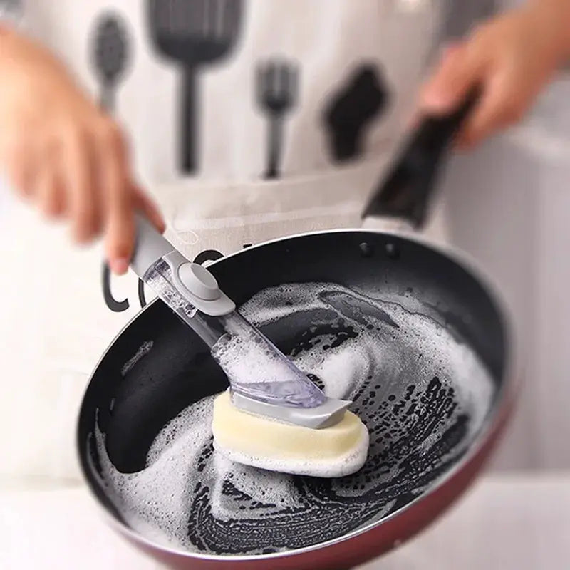 Refillable liquid cleaning brush with long handle and sponge by Simples Market scrubs a pan with dish soap.