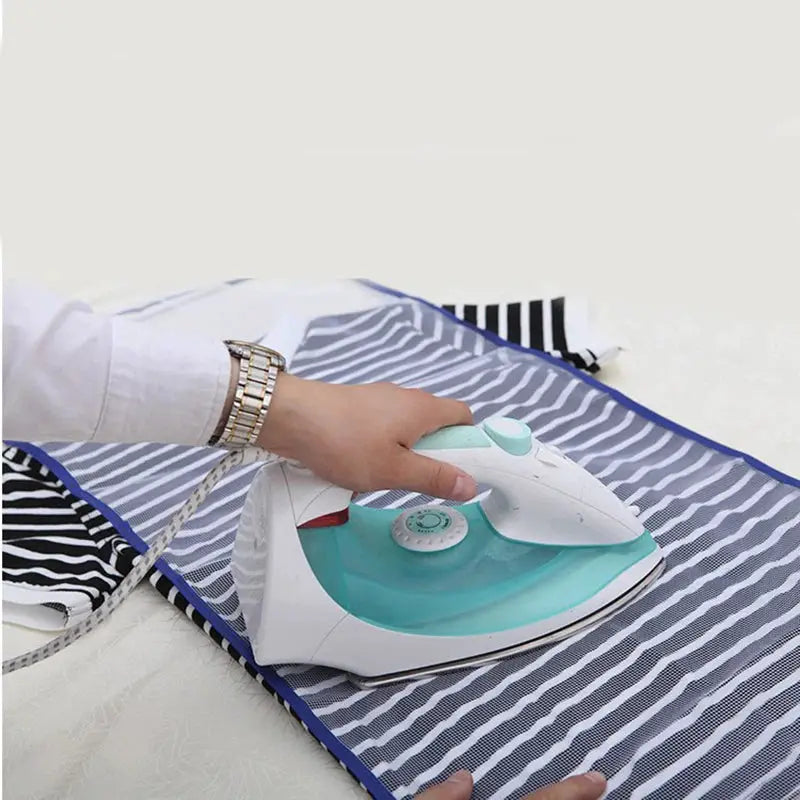 Clothes ironing protection pad on blue-bordered striped ironing board cover with a turquoise iron pressing down