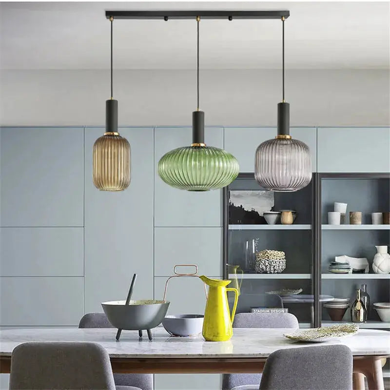Glass pendant lights set of three in amber, green and lilac hanging over a modern dining table.
