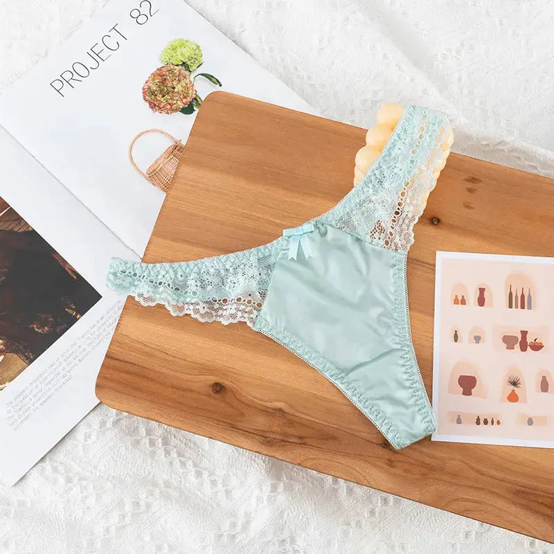 Light blue lace thong underwear with wide lace side panels on a wooden board