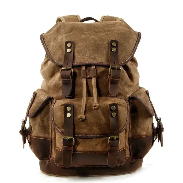 Vintage canvas backpack with brown leather straps and brass buckles; waxed mountaineering-style rucksack.