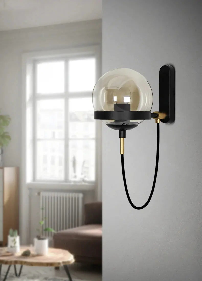 Modern glass ball wall lamp by Simples Market; black metal wall mount with a clear glass globe and brass accents