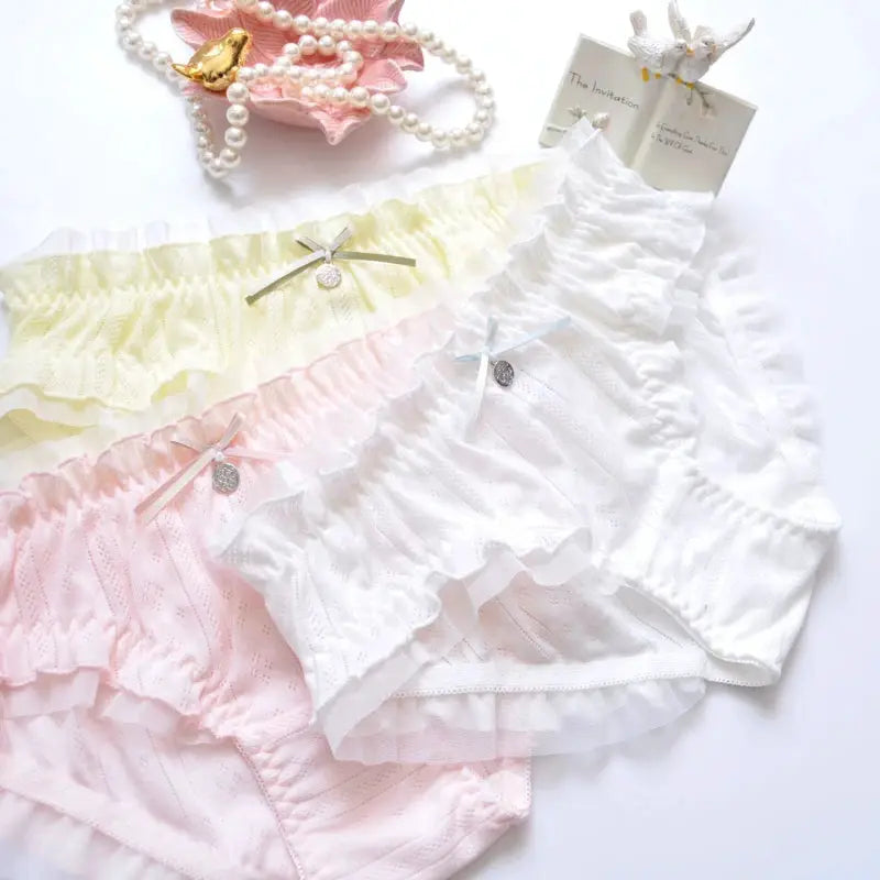 Set of three pastel cotton ruffle panties with bows in pink, yellow, and white.
