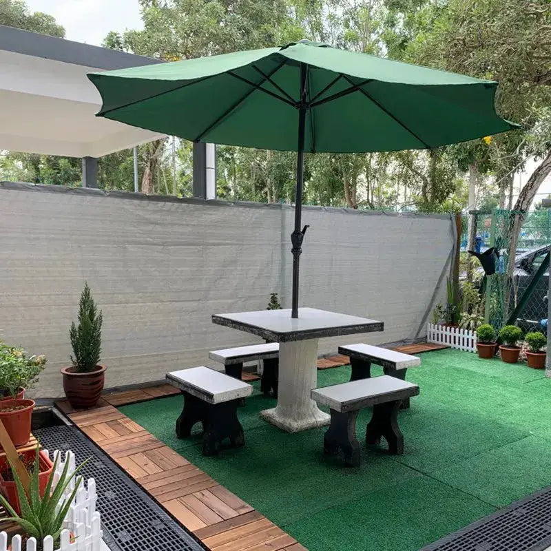 Patio umbrella with green canopy over a concrete pedestal table and matching benches in a backyard.