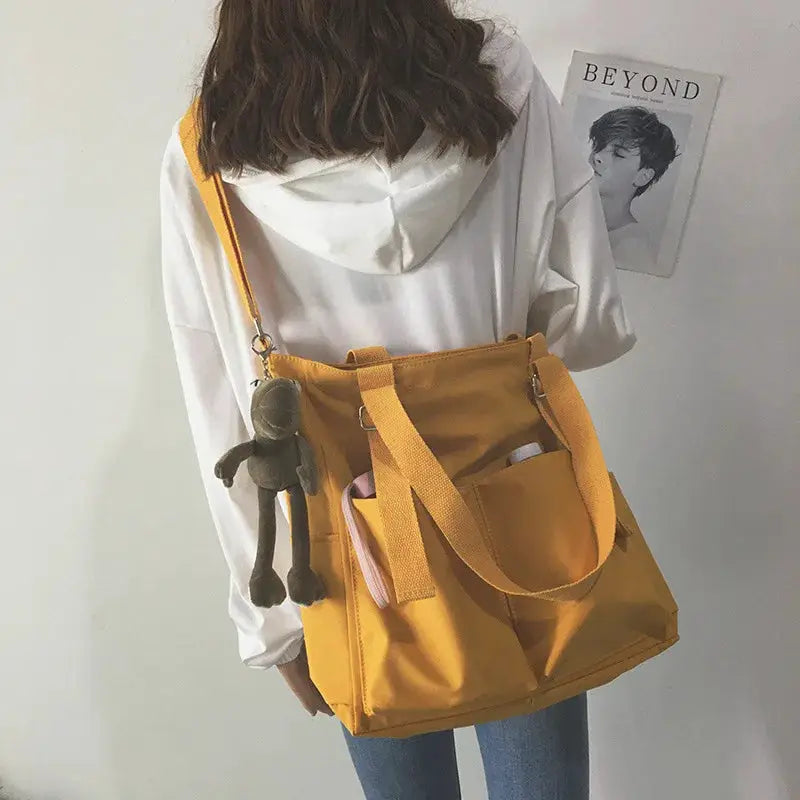 Waterproof Oxford large-capacity yellow handbag with shoulder strap and top handles, featuring a small gray plush keychain.